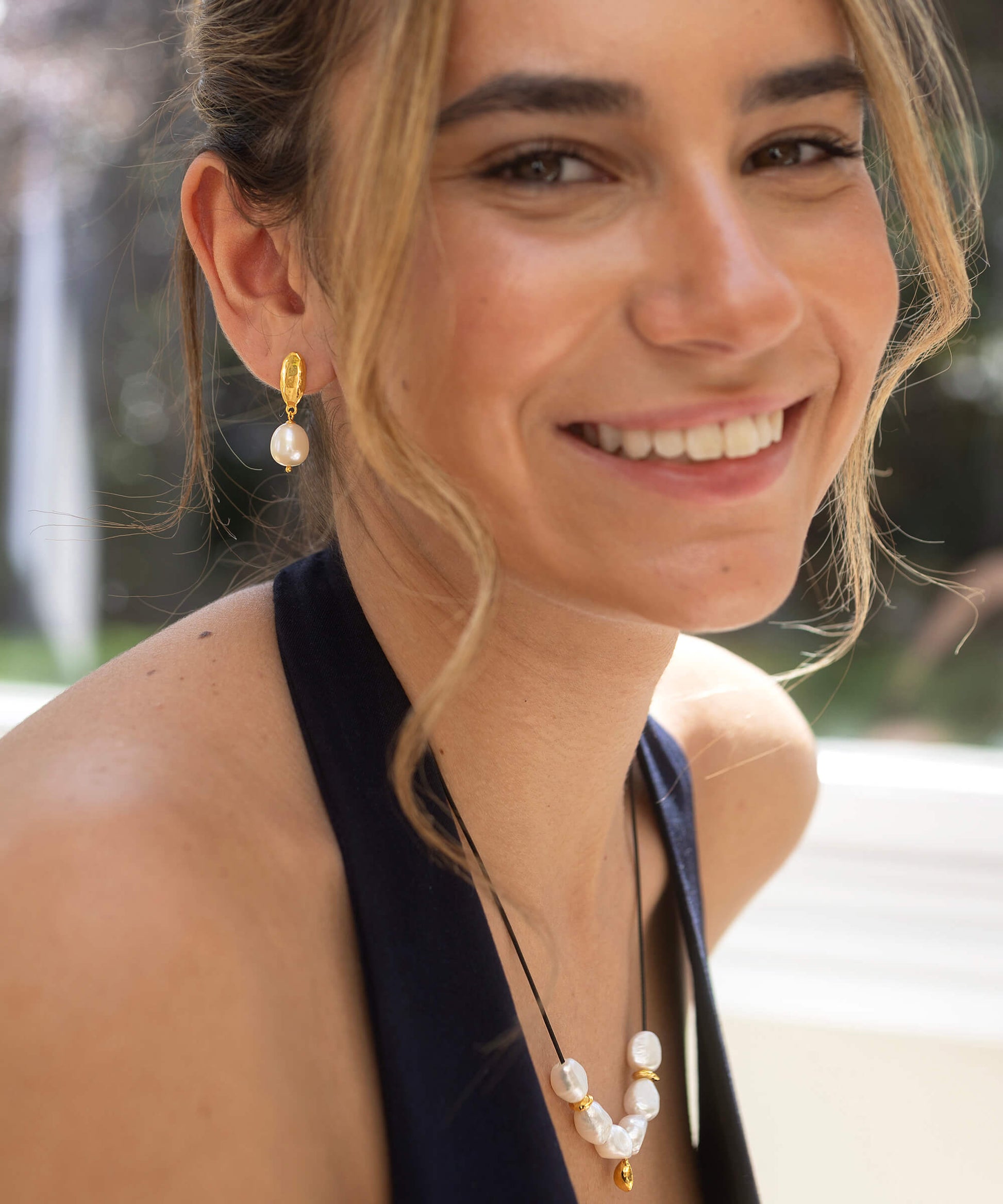 Woman wearing pearl earrings and necklace with blurred outdoor background