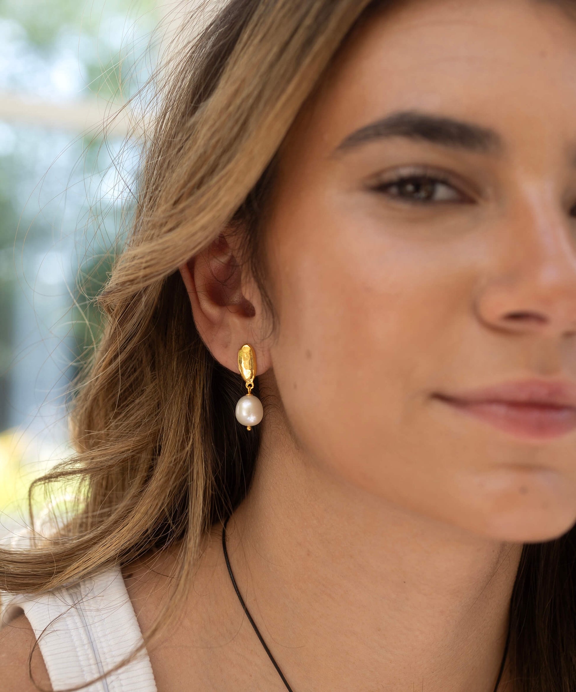 Close-up of a woman wearing gold earrings with a blurred outdoor background