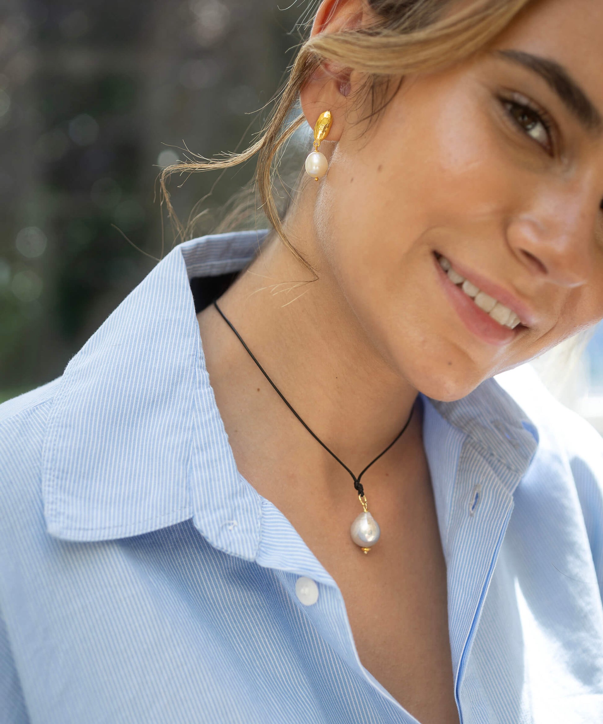 Woman wearing a pearl earring and necklace, smiling outdoors.