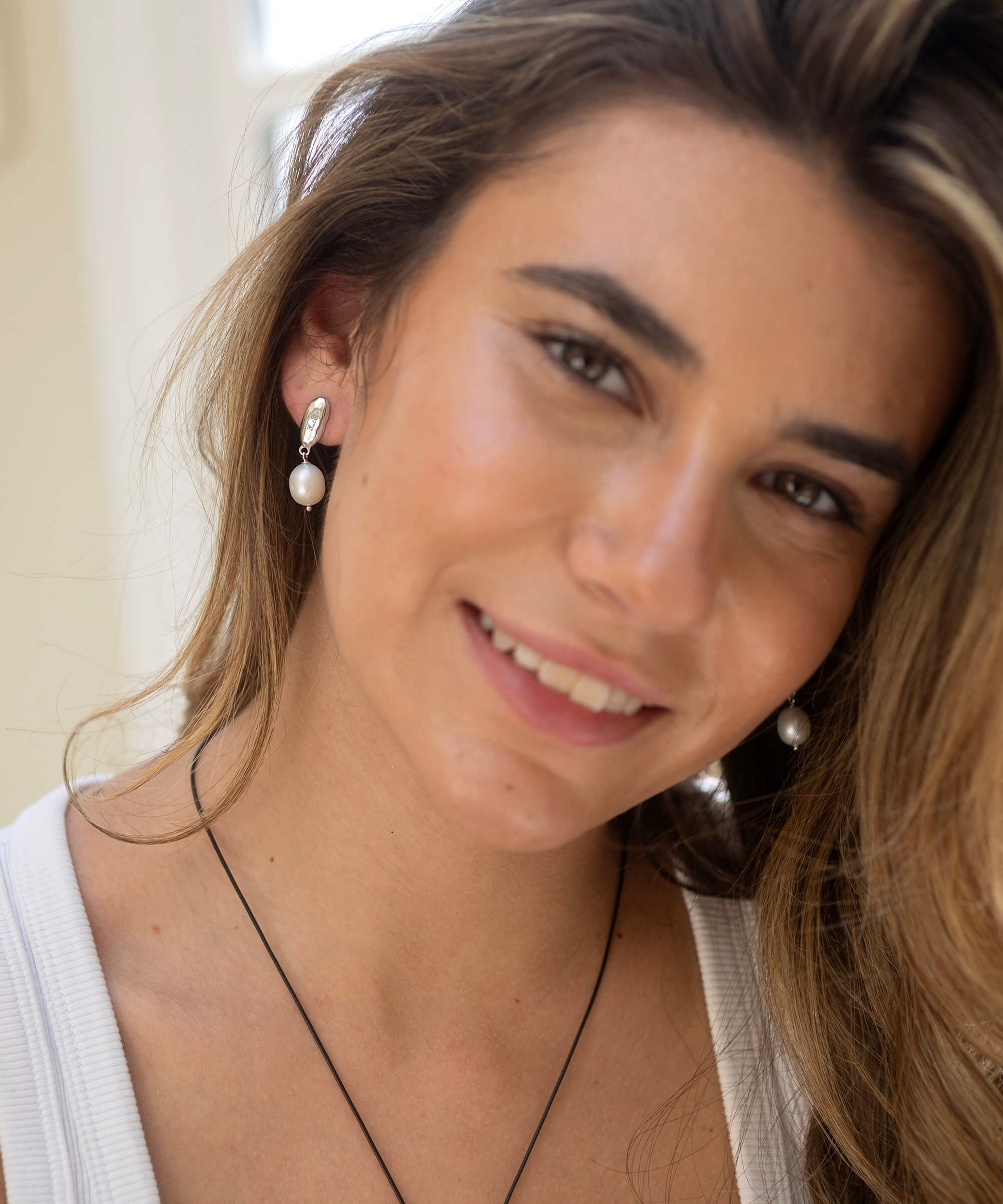Close-up of a woman wearing pearl earrings with a neutral background
