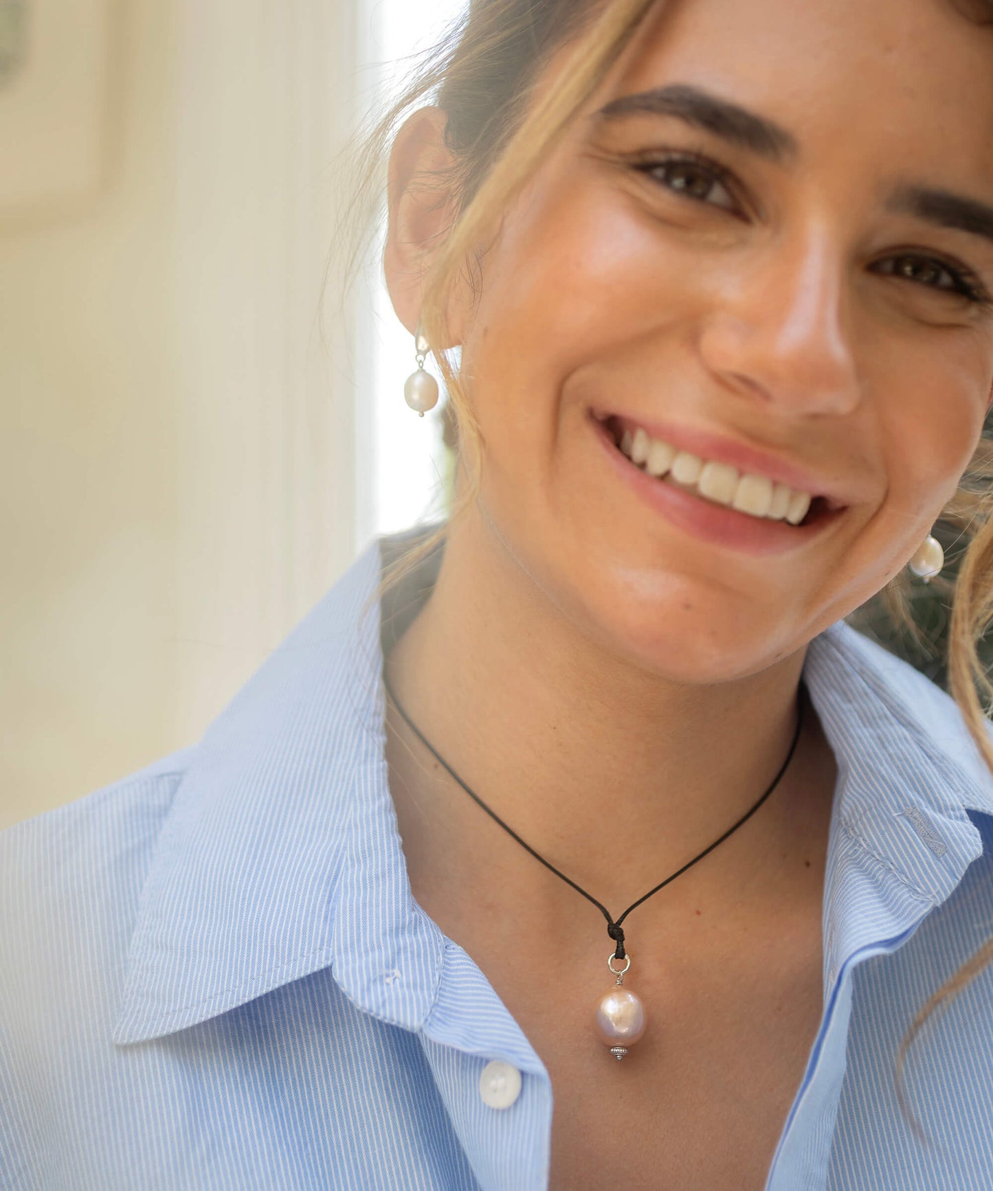 Woman wearing a light blue shirt and pearl necklace with matching earrings.