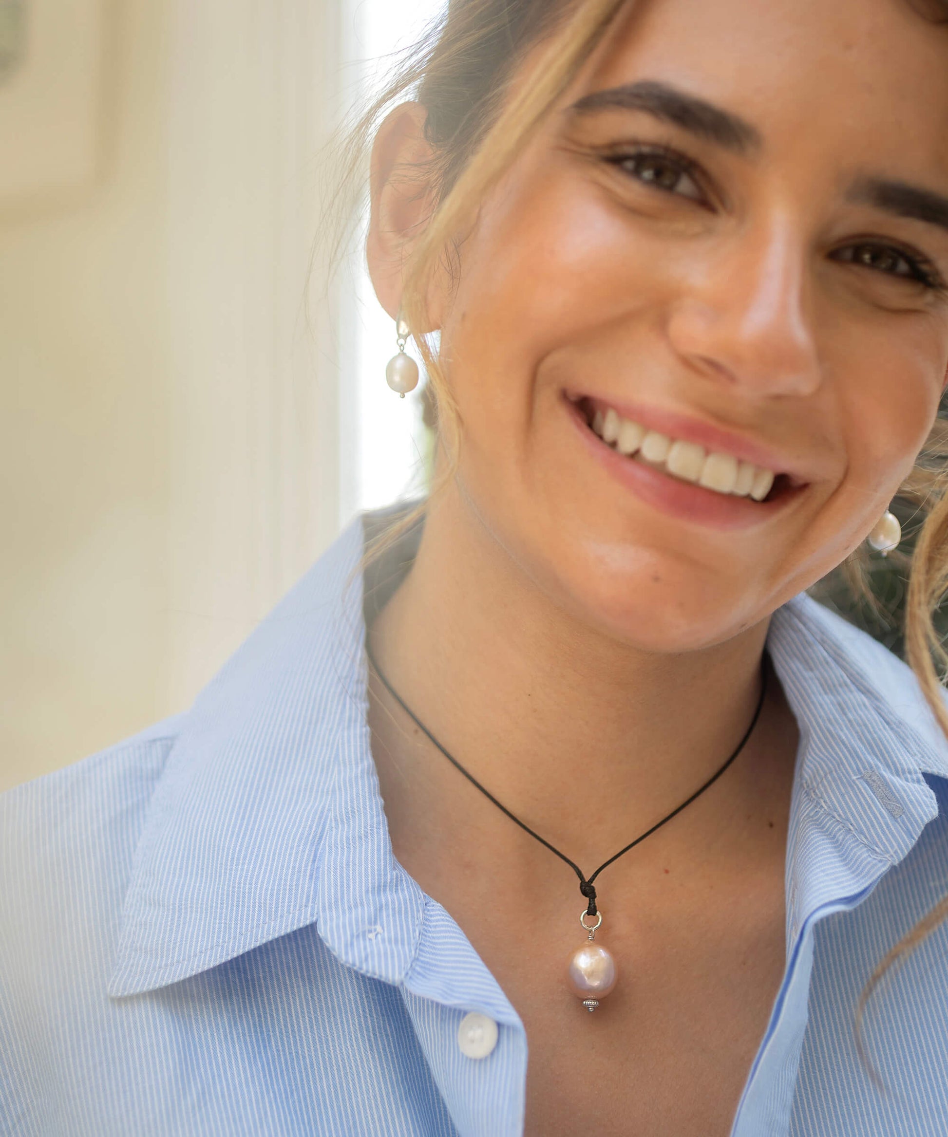 Woman wearing a light blue shirt and pearl necklace with matching earrings.