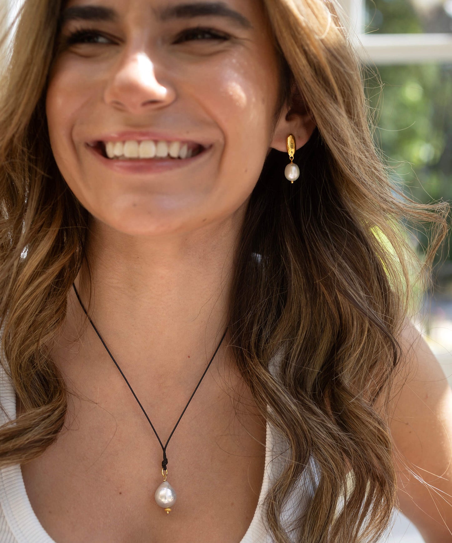 Woman wearing pearl earrings and a necklace with a blurred outdoor background