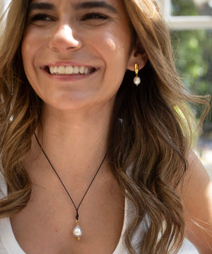 Woman wearing pearl earrings and a necklace with a blurred outdoor background