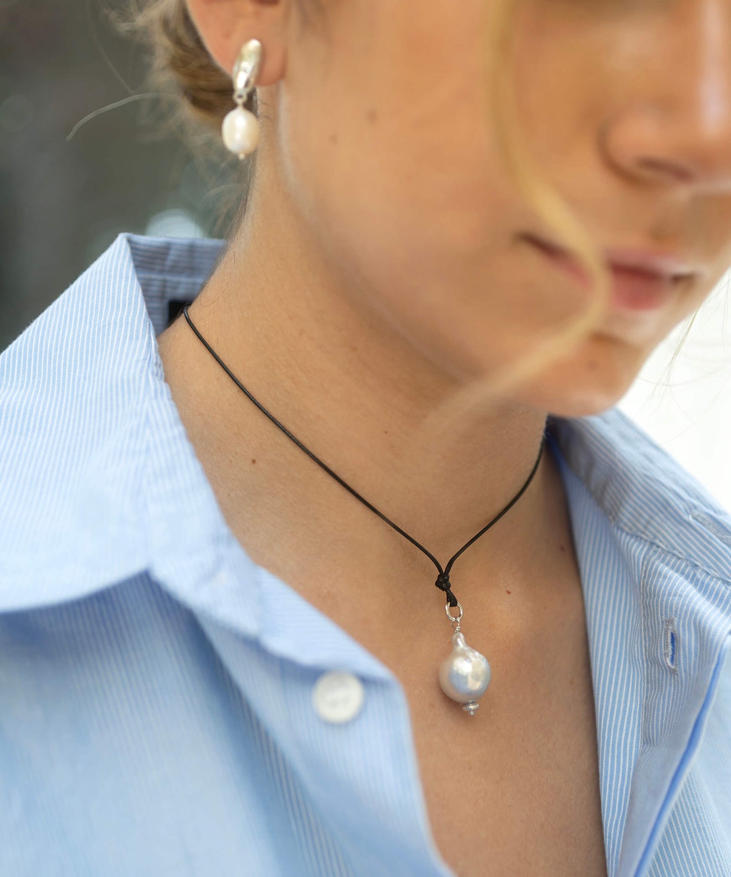 Close-up of a person wearing a pearl necklace and earrings with a blurred background