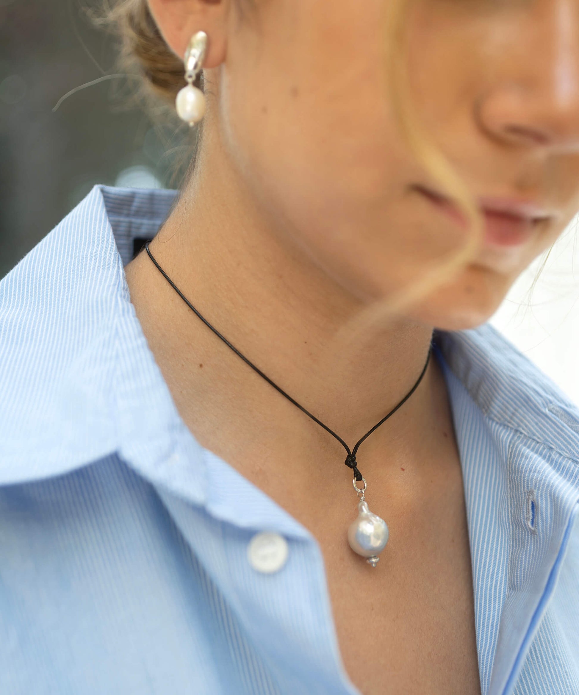 Close-up of a person wearing a pearl necklace and earrings with a blurred background