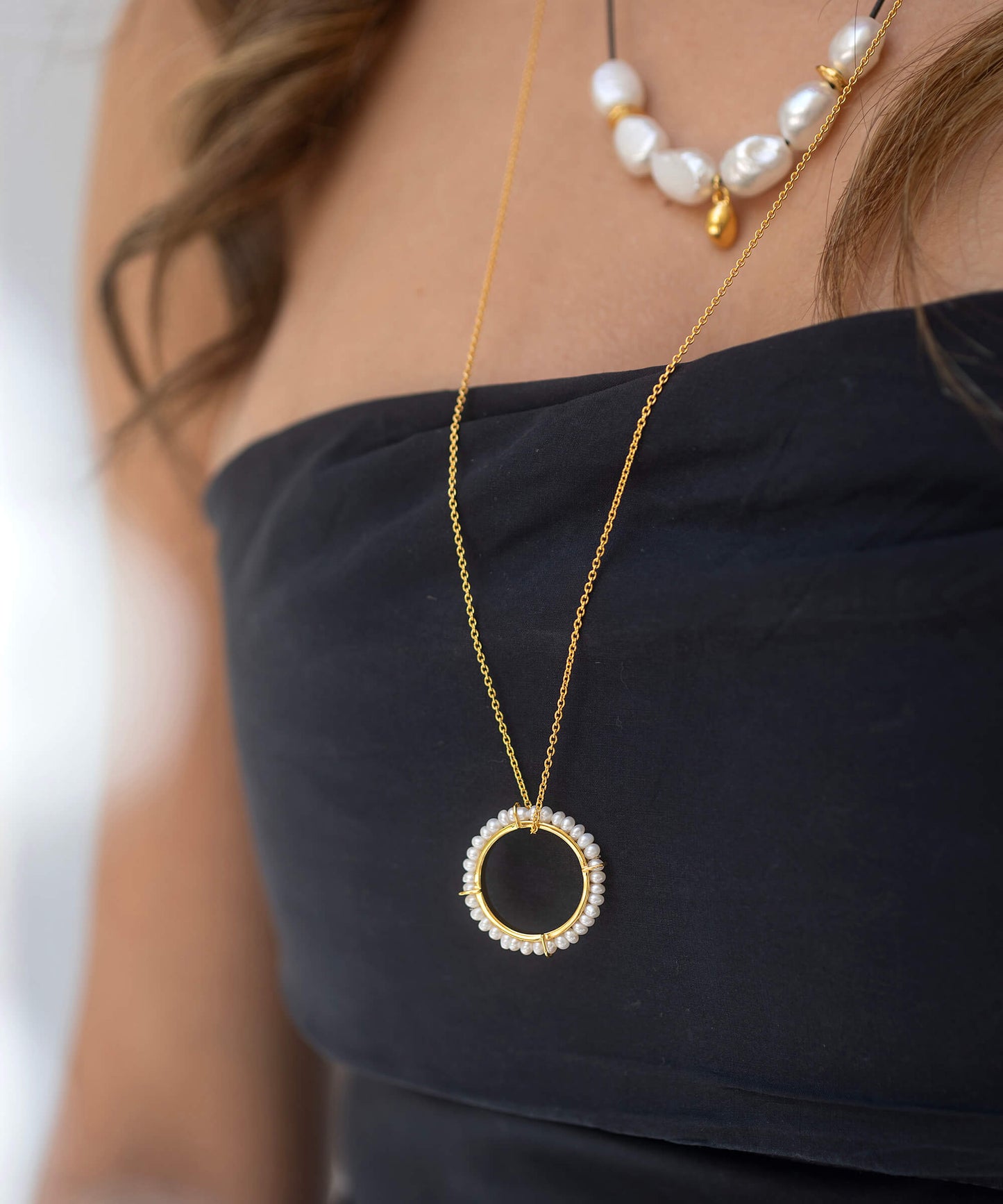 Gold necklace with a circular pendant worn by a person against a neutral background