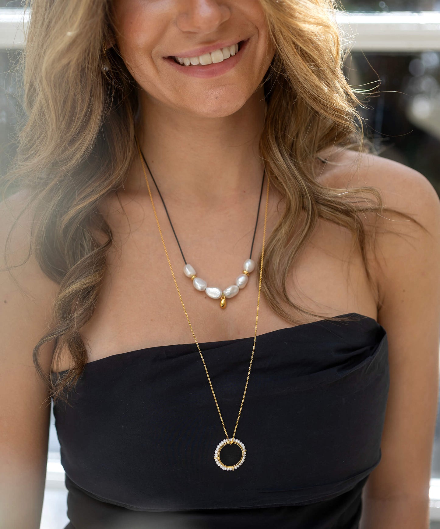 Woman wearing a black strapless top and pearl necklace with a blurred background