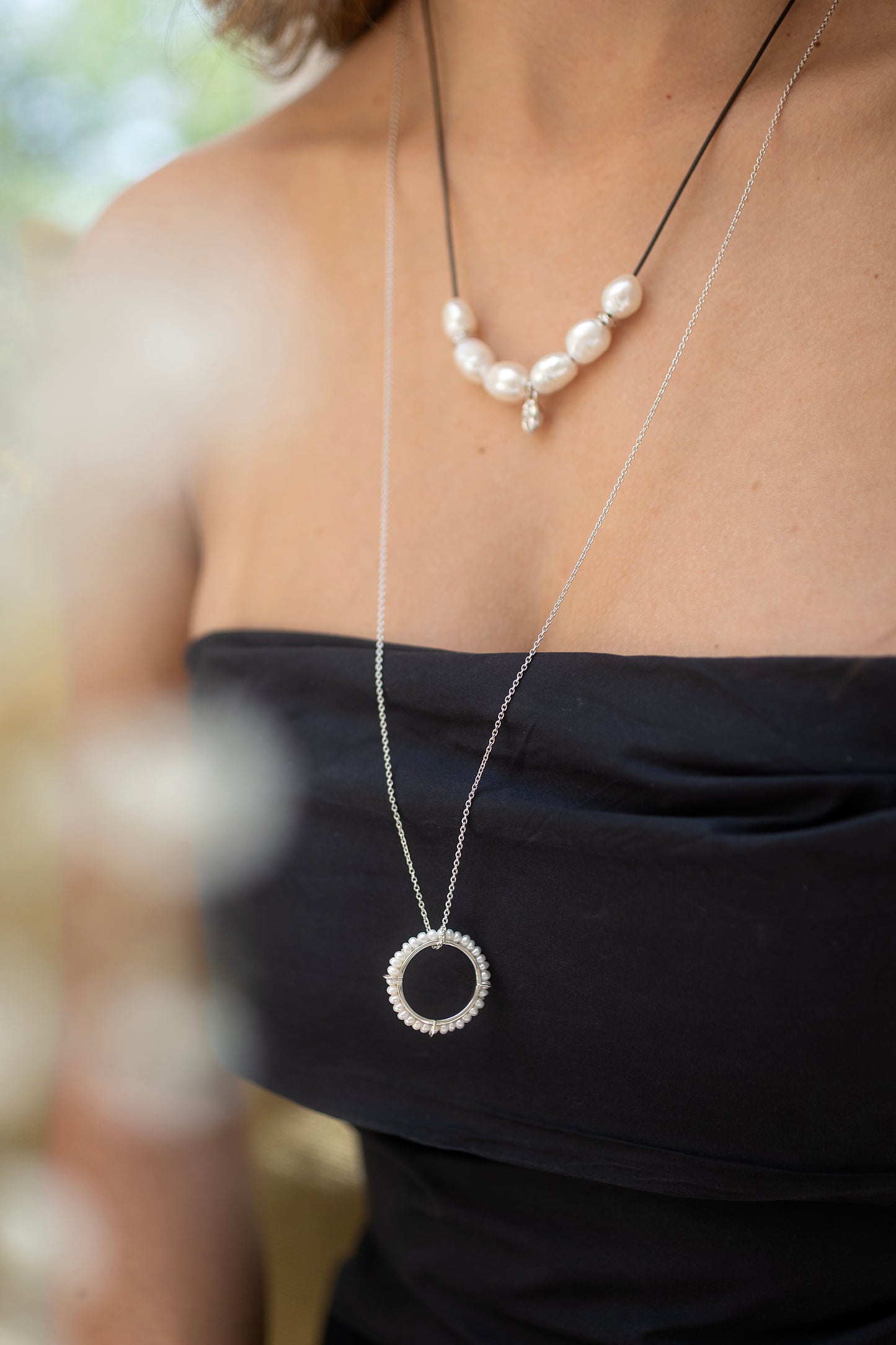 Close-up of a person wearing two necklaces with pearls and a circular pendant.