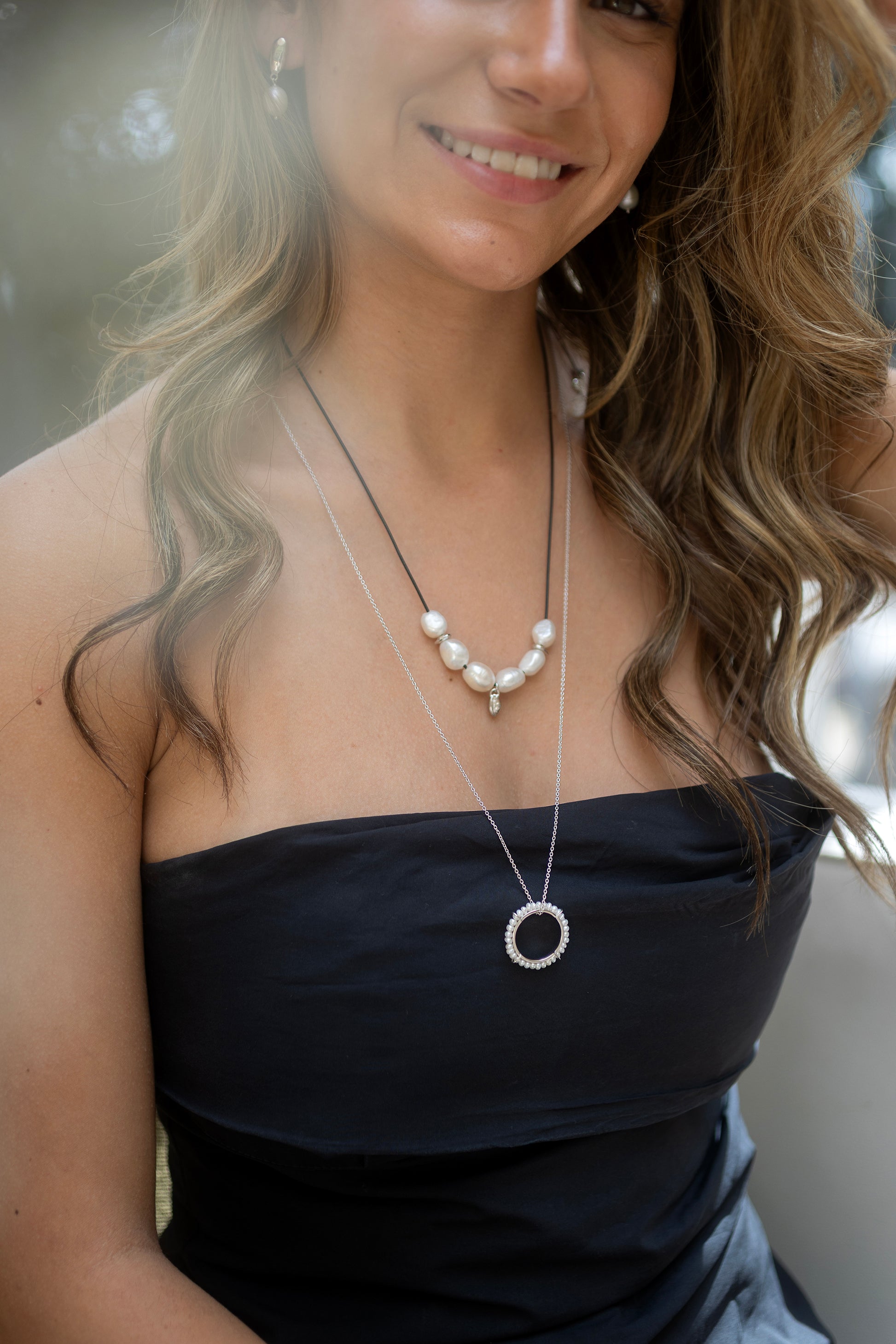 Woman wearing a black strapless top and pearl necklace with a blurred background